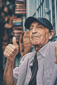older man in a baseball cap gives a thumbs up